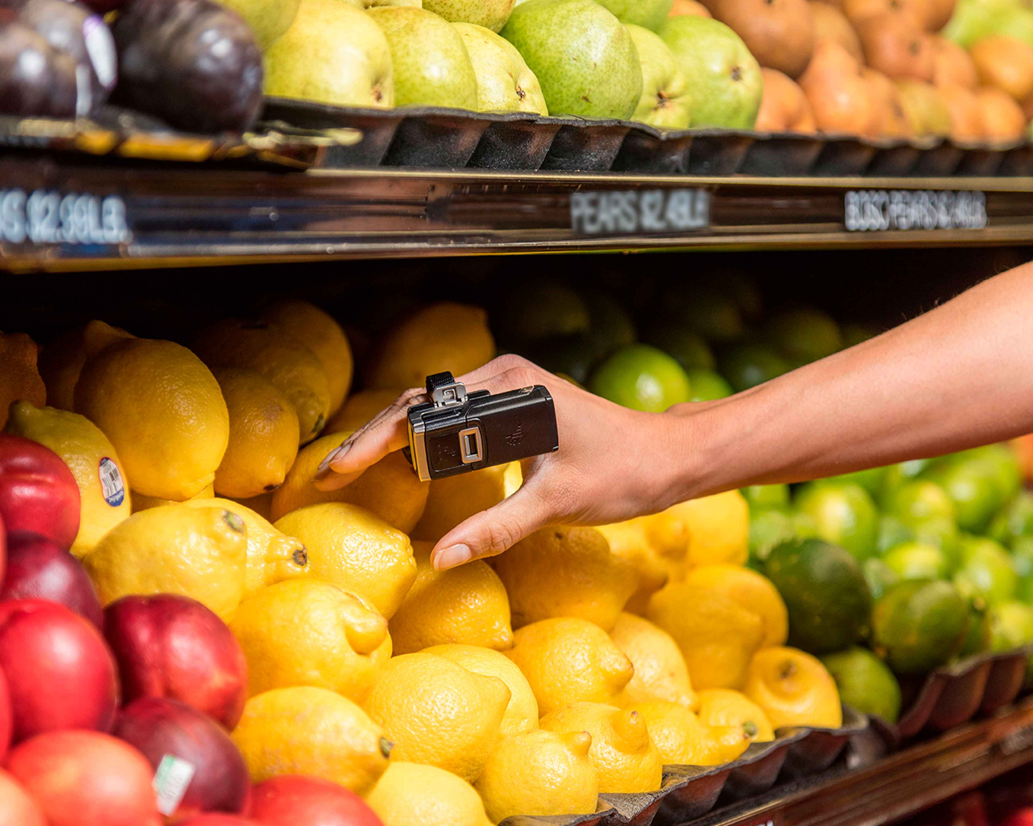 Grocery store worker wears Zebra RS5100 wireless Bluetooth barcode scanner on her index finger as she collects a lemon